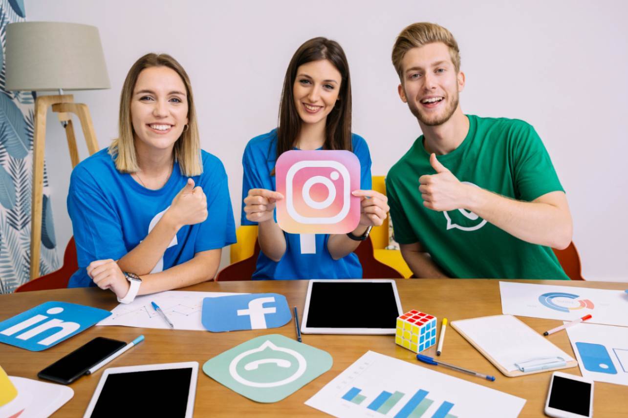 Three people holding Instagram logo with social media icons and marketing tools on table, representing Instagram content creation and digital marketing strategy.