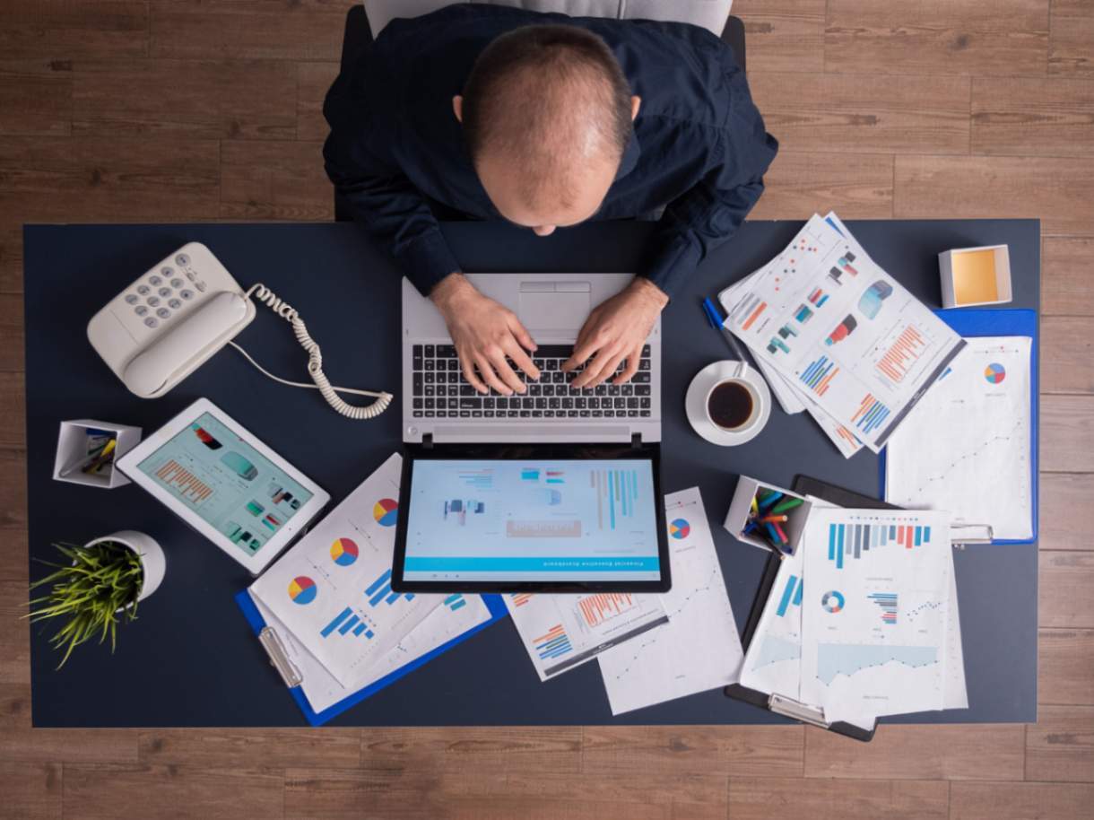 A professional businessman seated at a desk in a corporate office, typing on a laptop.